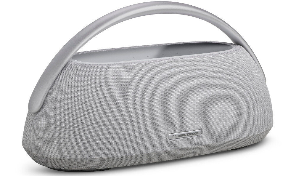 Na obrazie widoczny jest głośnik mobilny w kolorze szarym z zaokrąglonym uchwytem. Na przedniej części znajduje się logo \'harman/kardon\'.