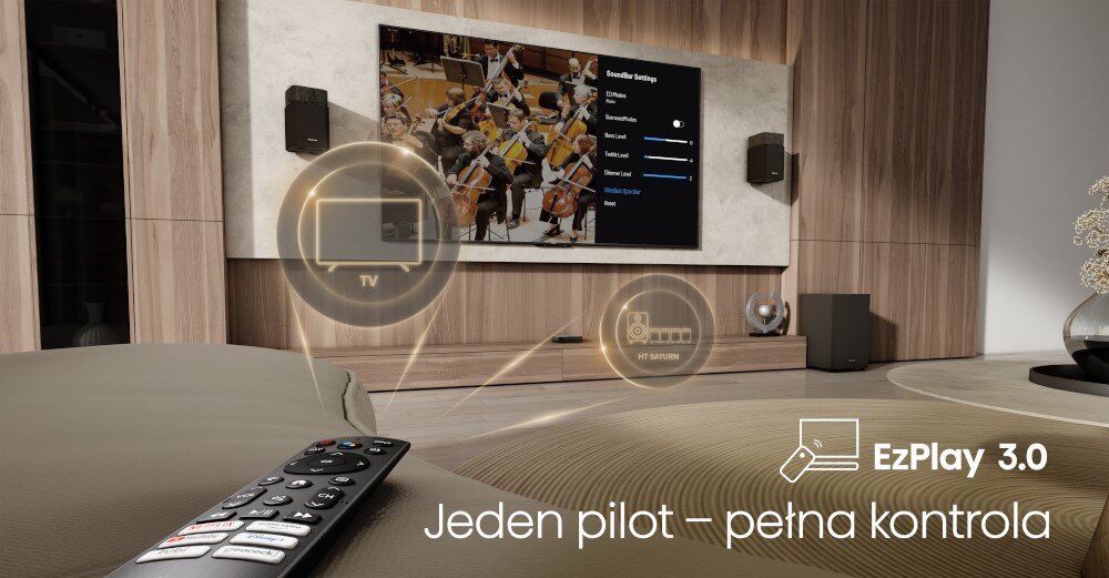 W salonie znajduje się telewizor z wyświetlonym menu ustawień dźwięku oraz dwa głośniki na ścianie. Na pierwszym planie widoczny jest pilot, a na ekranie napis \'Jeden pilot — pełna kontrola\'.