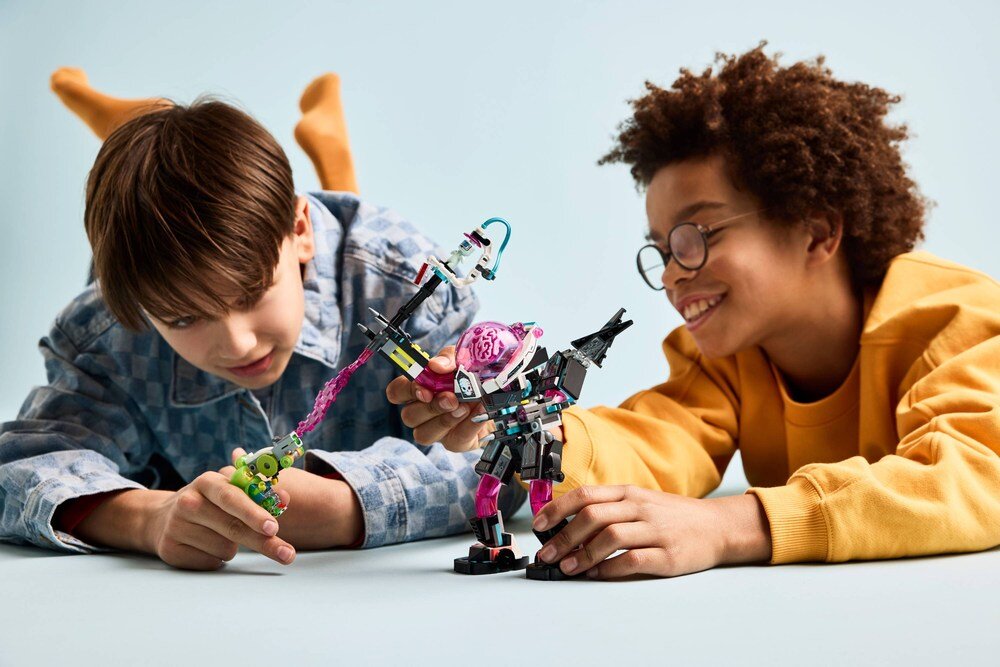 Dwóch chłopców bawi się zestawem LEGO, który przedstawia robota z różowym elementem przypominającym mózg. Chłopcy są uśmiechnięci i skupieni na zabawie.