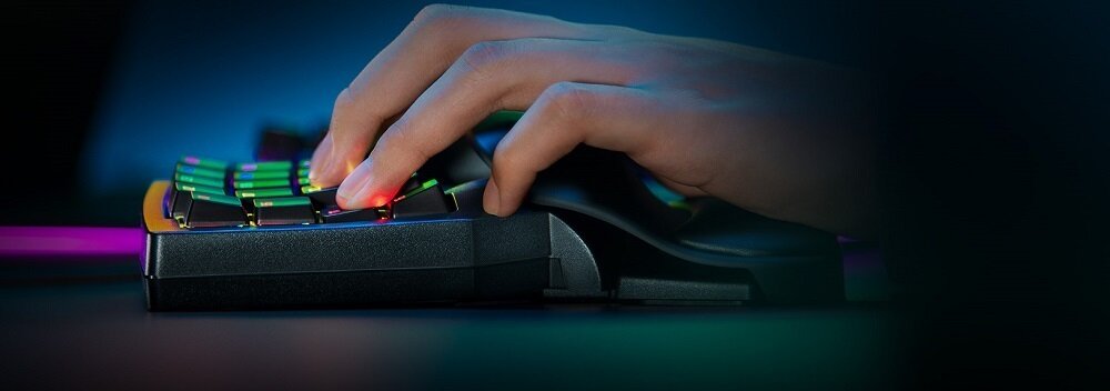 Na obrazie widać dłoń naciskającą klawisze urządzenia z podświetleniem RGB. Urządzenie ma czarną obudowę i jest używane w ciemnym otoczeniu.