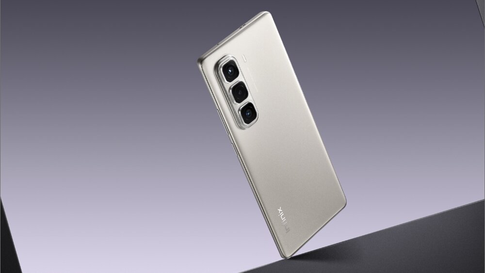 Na obrazie widoczny jest smartfon w kolorze srebrnym z trzema obiektywami aparatu na tylnej obudowie. Na obudowie znajduje się napis \'INFINIX\'.