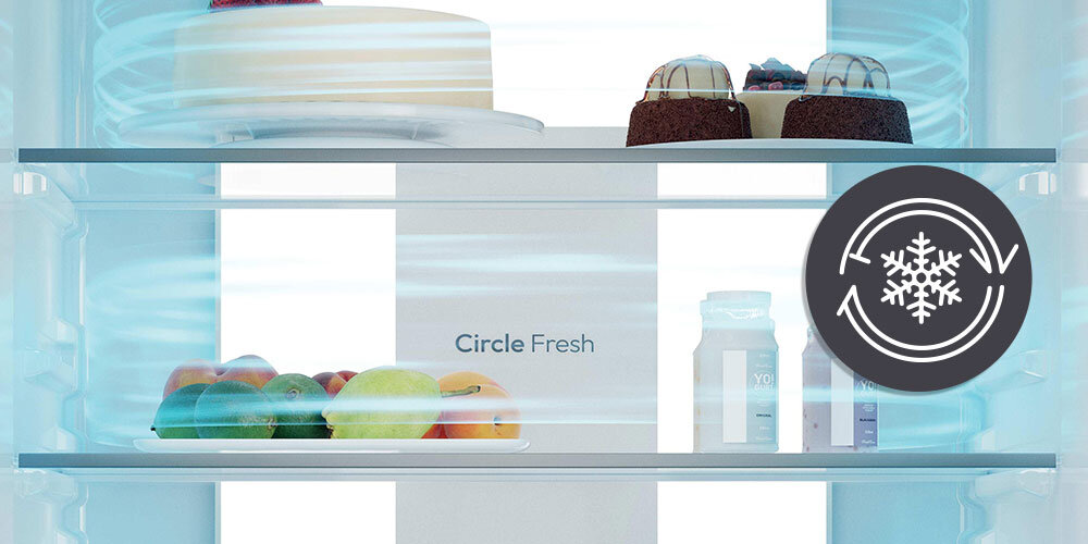 Wnętrze lodówki z widocznymi półkami, na których znajdują się owoce, ciasta i butelki. Na tylnej ściance widoczny jest napis \'Circle Fresh\' oraz symbol z płatkiem śniegu i strzałkami.