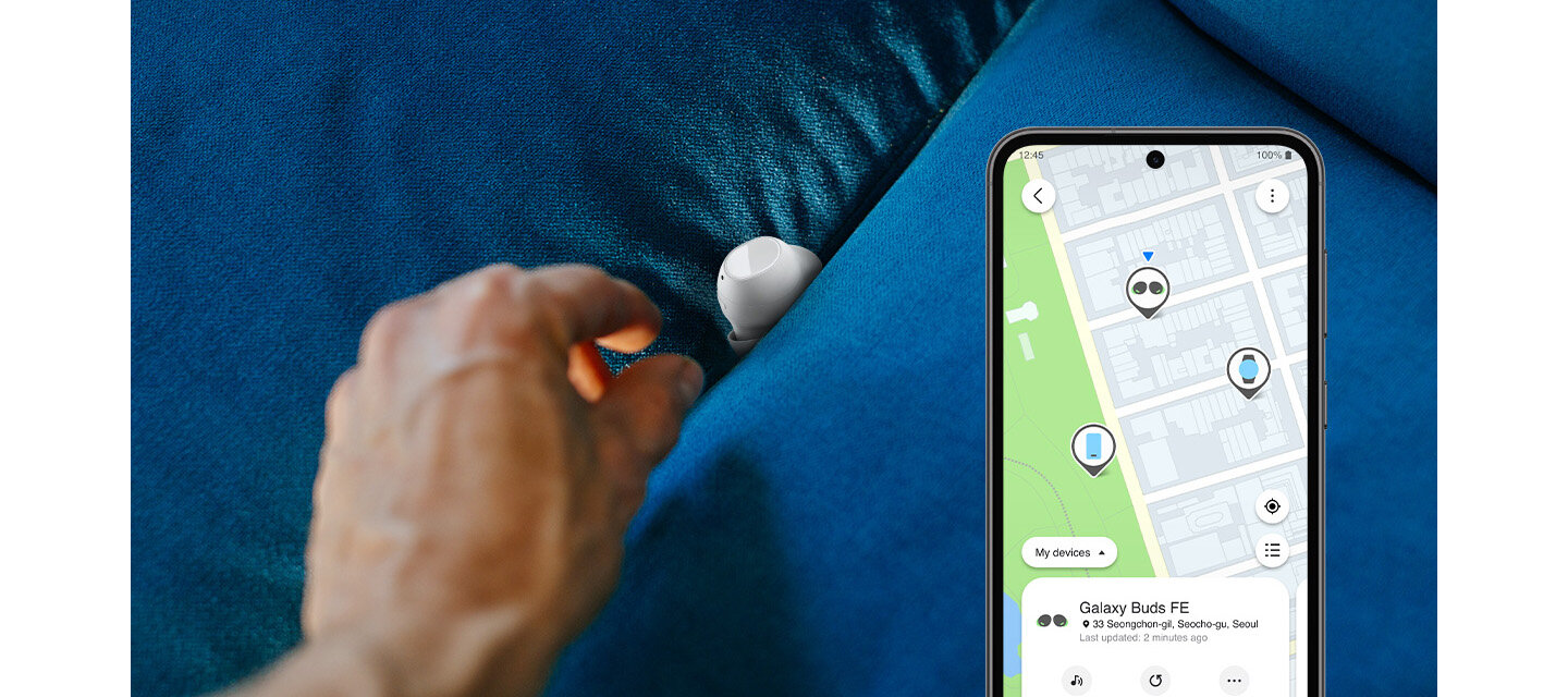 Na niebieskiej kanapie leży biała słuchawka dokanałowa, obok której znajduje się dłoń. Obok widoczny jest smartfon z mapą i lokalizacją oznaczoną jako \'Galaxy Buds FE\'.