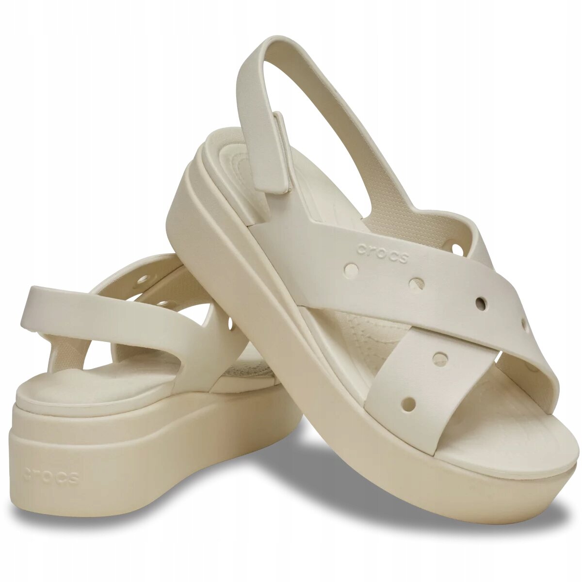 Na obrazie widoczne są beżowe sandały z grubą podeszwą i paskami krzyżującymi się na przodzie. Na jednym z pasków widnieje napis \'crocs\'.