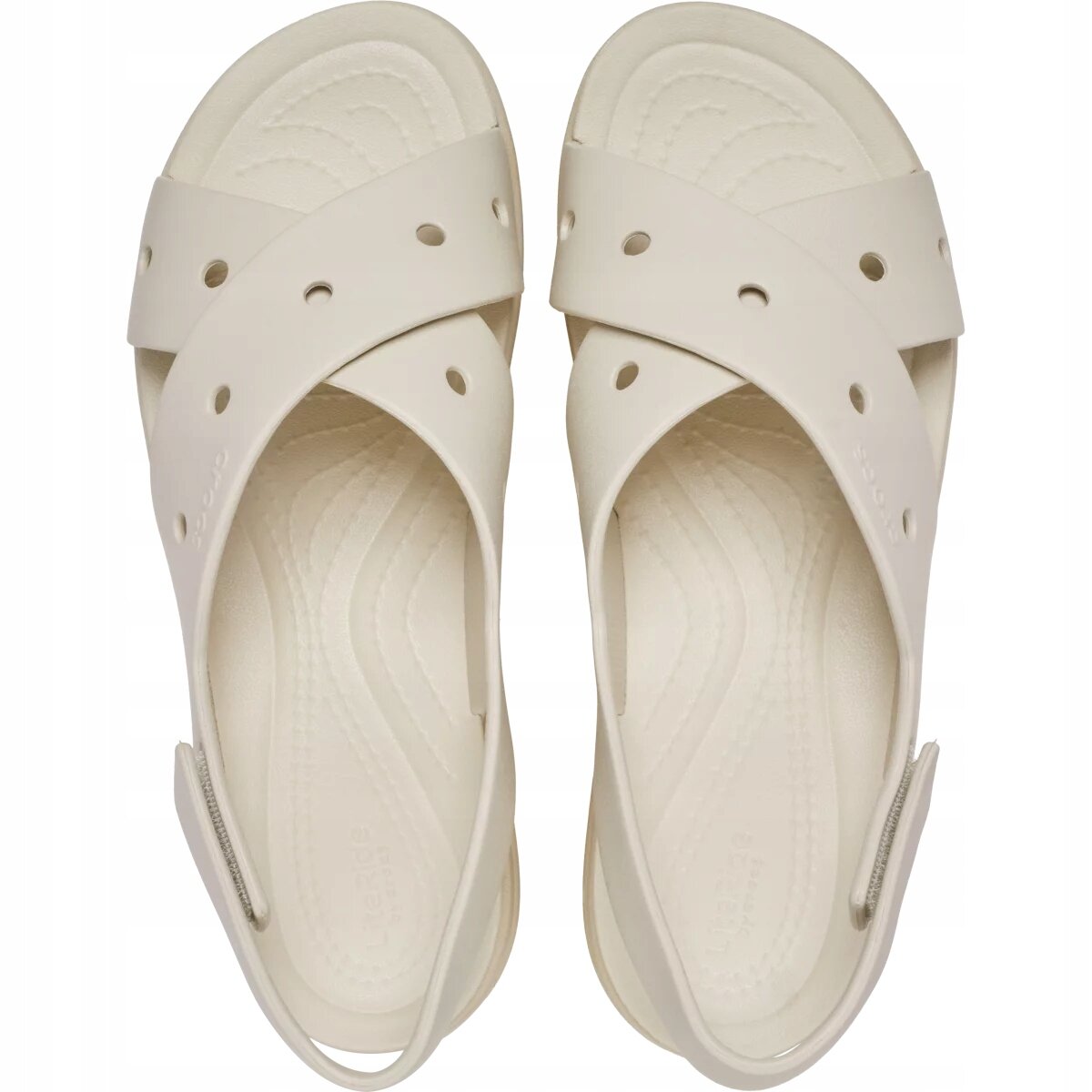 Para beżowych sandałów z krzyżującymi się paskami i otworami na górze. Wkładka ma delikatny wzór falisty, a na jednym z pasków widoczne jest logo \'Crocs\'.