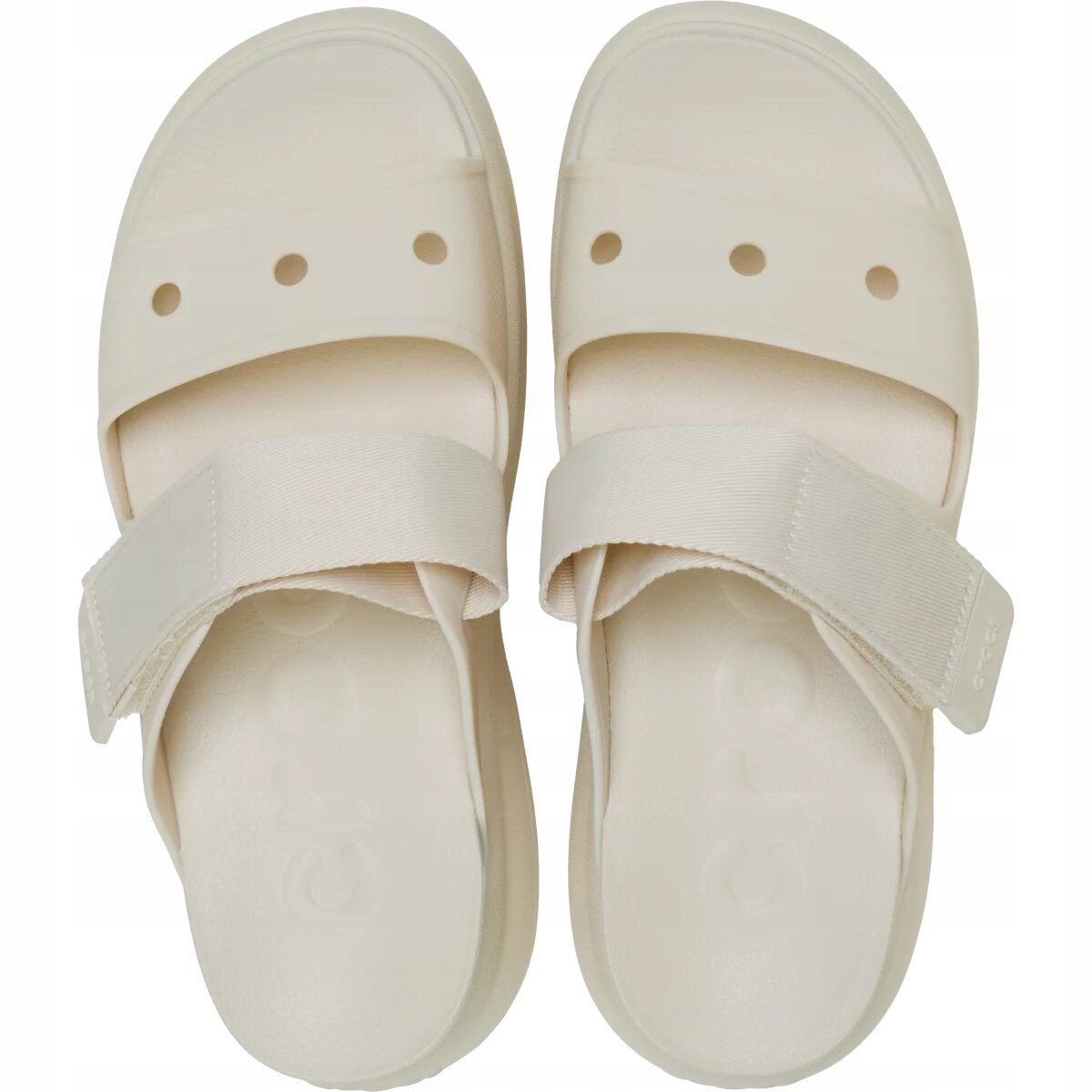 Para jasnych sandałów z dwoma paskami, z widocznymi otworami na jednym z pasków. Na jednym z pasków widoczny jest napis \'crocs\'.