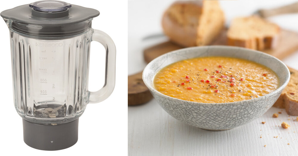 Po lewej stronie znajduje się szklany blender z miarką i ciemnoszarym wieczkiem. Po prawej stronie widoczna jest miska z zupą krem, ozdobiona przyprawami, a w tle leży chleb.