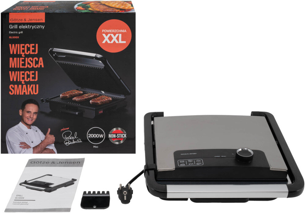 Na obrazie widoczny jest grill elektryczny z metalową pokrywą i pokrętłem na panelu sterowania. Obok znajduje się pudełko z napisem \'Götze & Jensen Grill elektryczny GL500X\', \'WIĘCEJ MIEJSCA WIĘCEJ SMAKU\', oraz broszura i akcesoria.