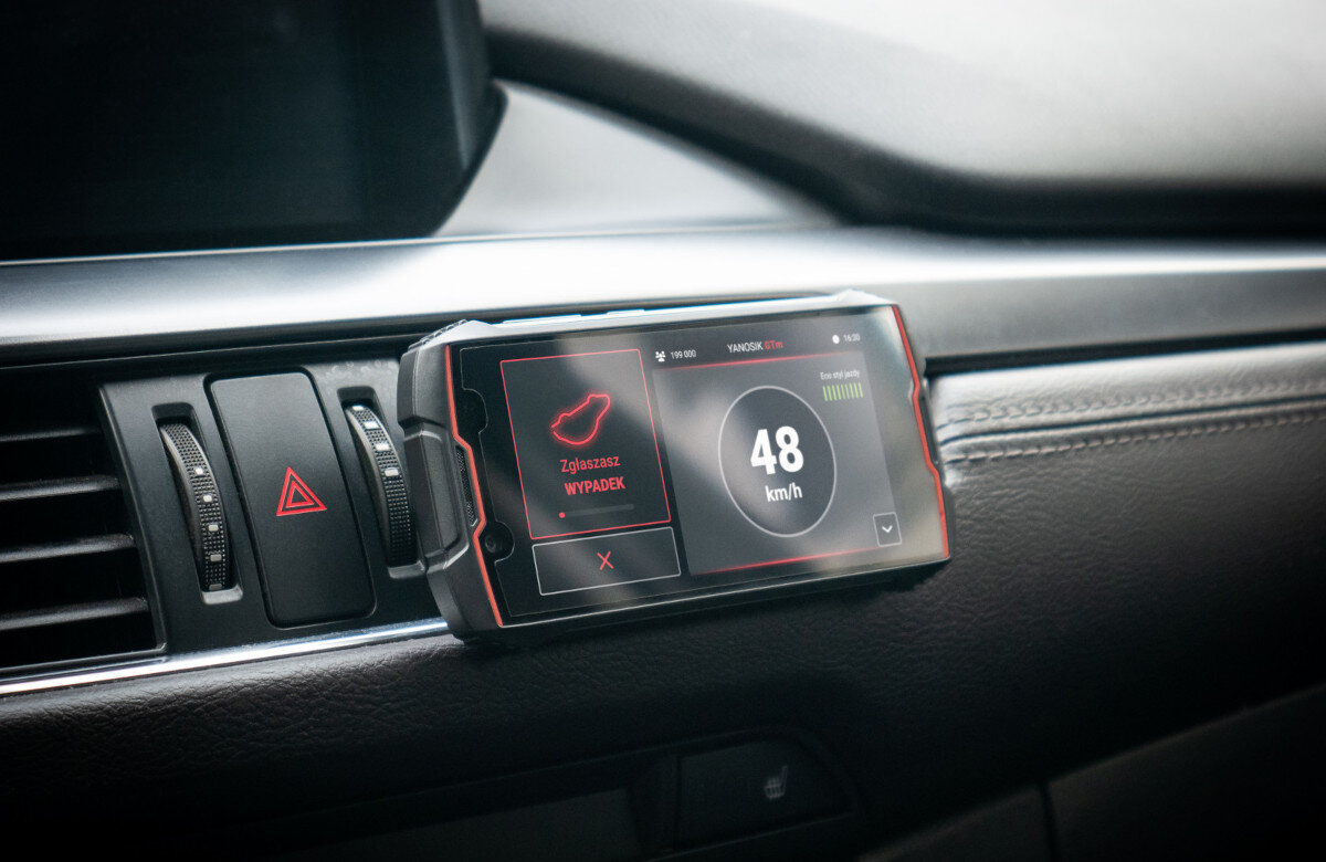 Na desce rozdzielczej samochodu zamontowany jest urządzenie z wyświetlaczem pokazującym prędkość 48 km/h oraz komunikat \'Zgłoszono WYPADKI\'.