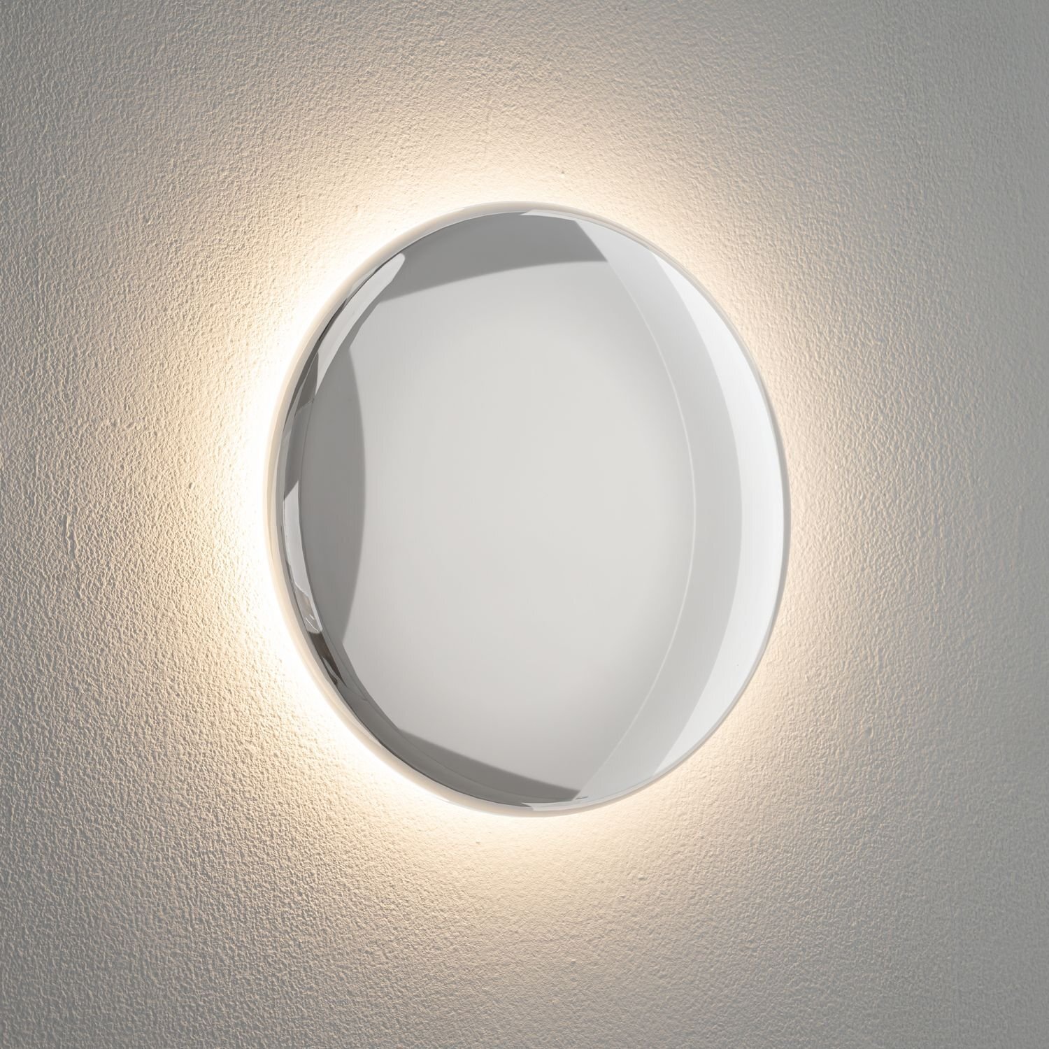 Na obrazie widoczna jest okrągła lampa ścienna emitująca delikatne światło na ścianę. Lampa ma gładką, błyszczącą powierzchnię.