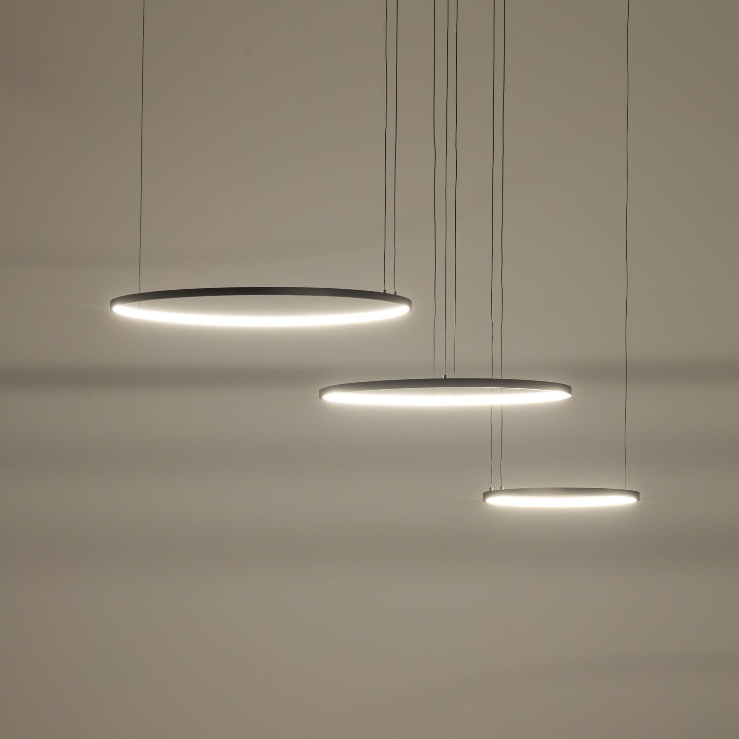 Na obrazie widoczne są trzy okrągłe, wiszące lampy LED o nowoczesnym designie, emitujące białe światło. Lampy zawieszone są na cienkich przewodach na tle jasnej ściany.