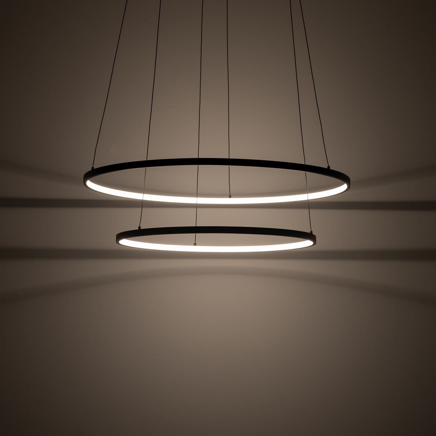 Na obrazie widoczne są dwie okrągłe, wiszące lampy LED emitujące ciepłe światło. Lampy są zawieszone na cienkich przewodach i tworzą nowoczesny, minimalistyczny wygląd.