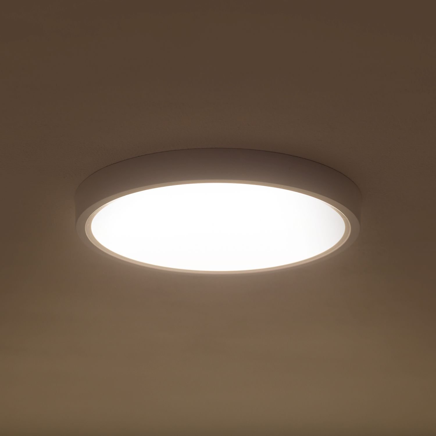 Na obrazie widoczny jest okrągły plafon LED zamontowany na suficie, emitujący jasne światło. Lampa ma prosty, nowoczesny design z białą obudową.