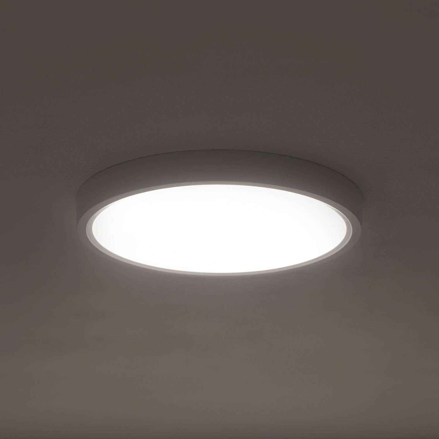 Na obrazie widoczny jest okrągły plafon LED zamontowany na suficie, emitujący jasne, białe światło. Plafon ma prosty, nowoczesny design z ciemną obudową.