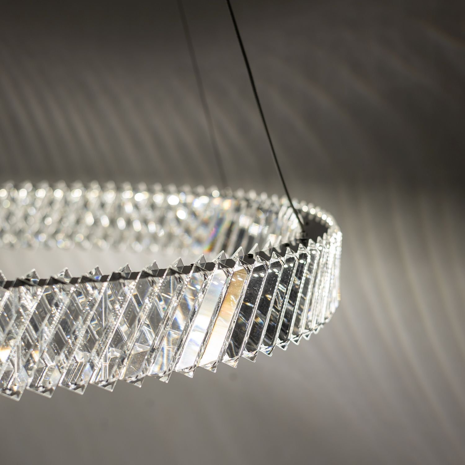 Lampa wisząca LED o nowoczesnym designie, złożona z przezroczystych, geometrycznych elementów tworzących okrągły kształt. Światło tworzy efektowne wzory na otaczającej powierzchni.