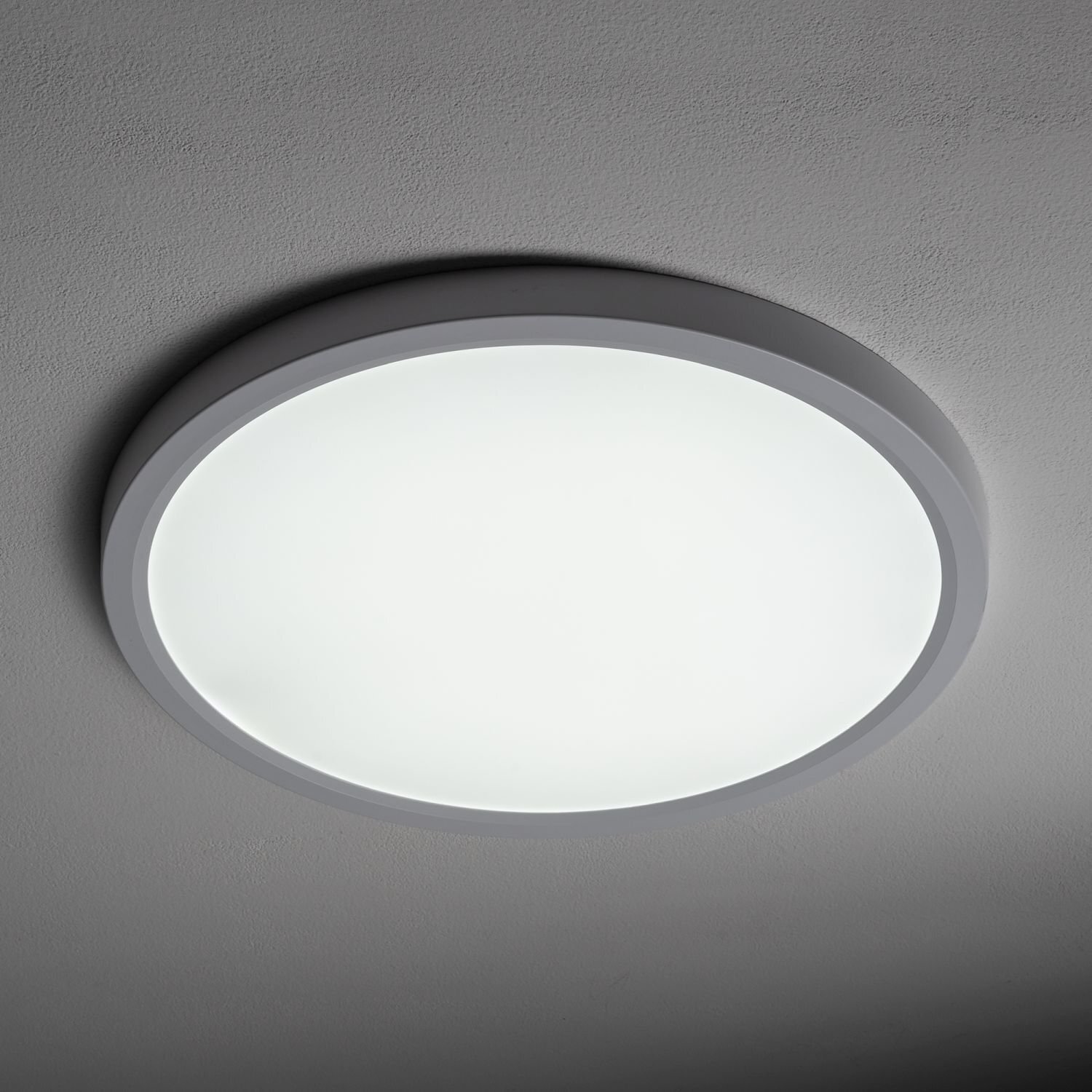 Na obrazie widoczny jest okrągły plafon LED zamontowany na suficie, emitujący jasne, białe światło. Plafon ma prosty, nowoczesny design z cienką ramką.