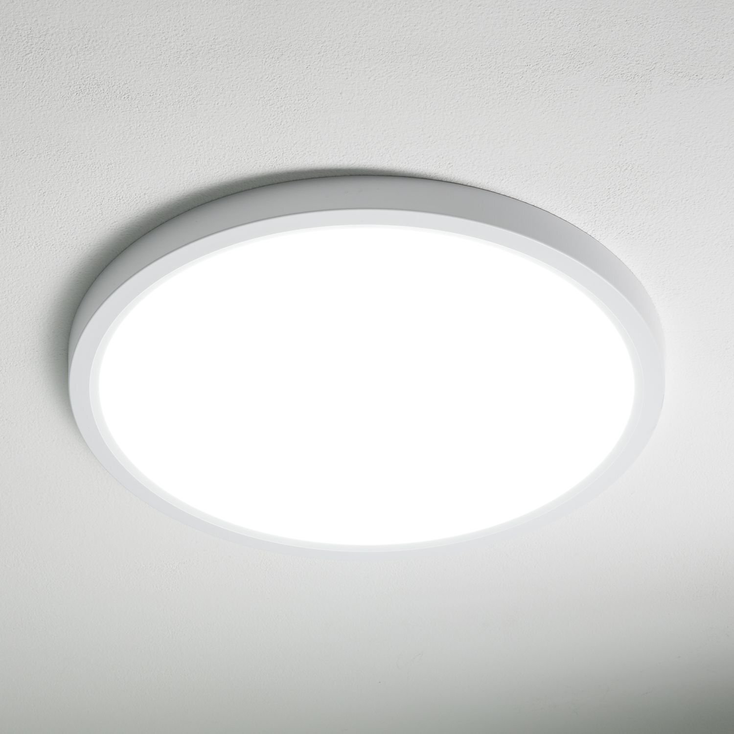 Na obrazie widoczny jest okrągły plafon LED zamontowany na suficie, emitujący jasne, białe światło. Lampa ma prosty, nowoczesny design z białą obudową.