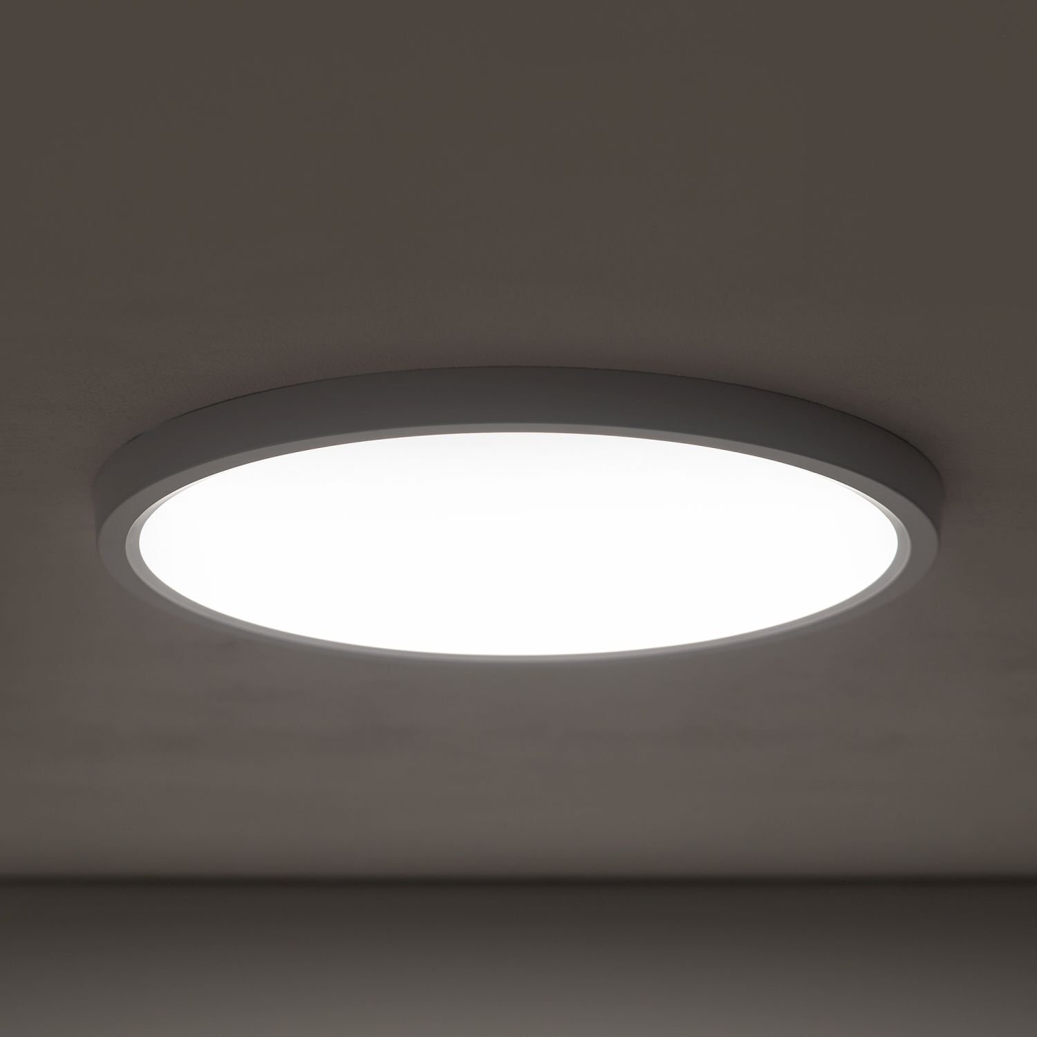 Na obrazie widoczny jest okrągły plafon LED zamontowany na suficie, emitujący jasne, białe światło. Lampa ma prosty, nowoczesny design z cienką ramką.