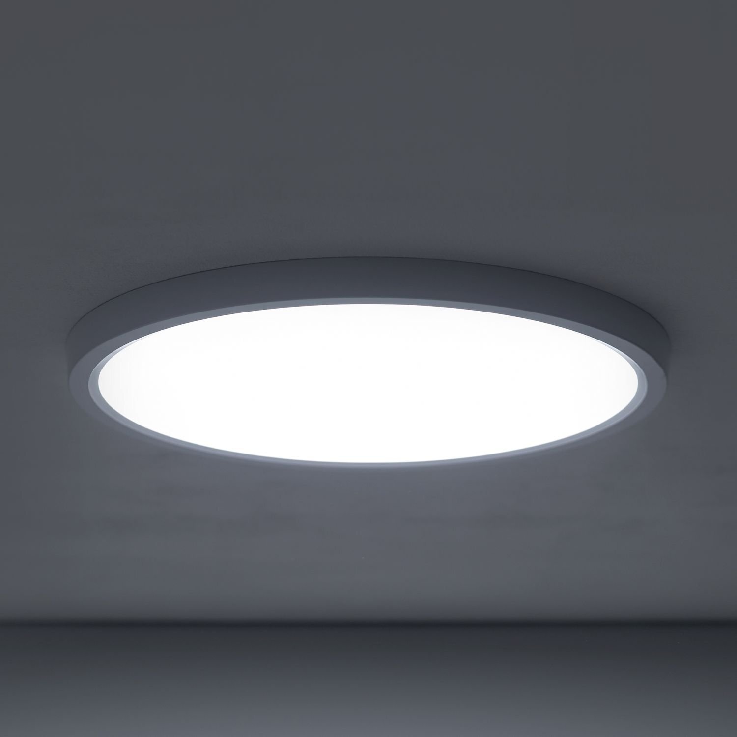 Na obrazie widoczny jest okrągły plafon LED zamontowany na suficie, emitujący jasne, białe światło. Lampa ma prosty, nowoczesny design z ciemną obwódką.