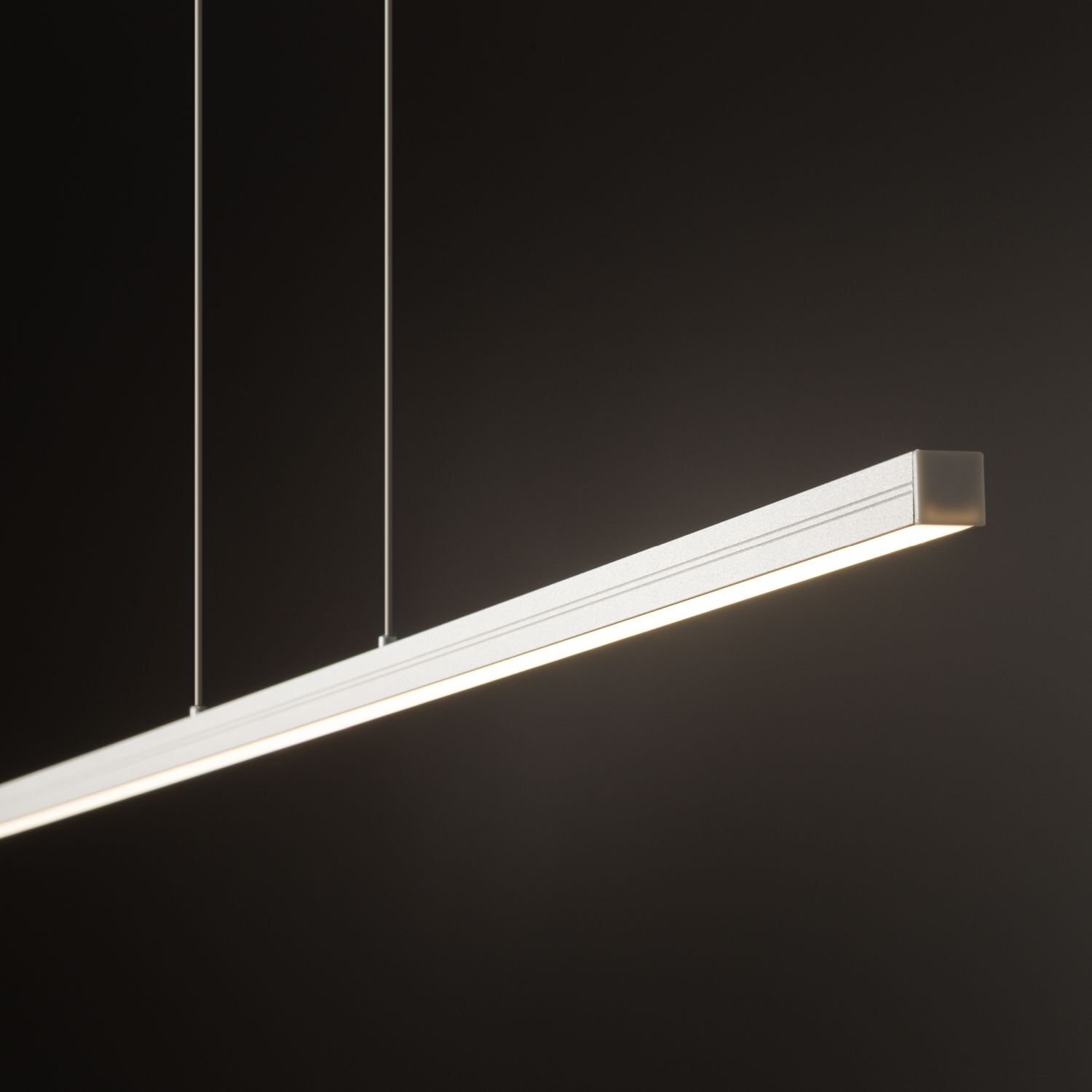 Nowoczesna lampa wisząca LED o prostokątnym kształcie, zawieszona na dwóch cienkich przewodach, emitująca jasne światło. Tło jest ciemne, co podkreśla minimalistyczny design lampy.