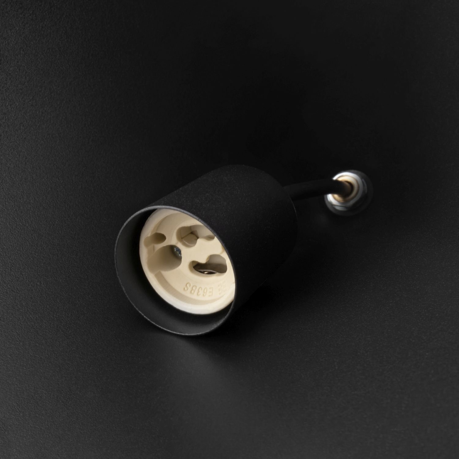 Zbliżenie na czarną oprawkę lampy z widocznym gniazdem żarówki w kolorze kremowym. Tło jest również czarne, co podkreśla elegancki design produktu.