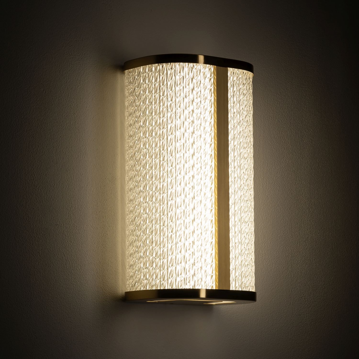 Lampa ścienna LED o nowoczesnym designie, z ozdobnym wzorem na powierzchni, emitująca ciepłe światło. Obudowa lampy jest w kolorze złotym.