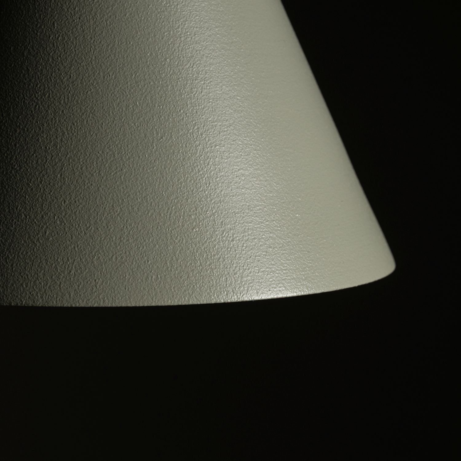Obraz przedstawia zbliżenie na powierzchnię klosza lampy o teksturowanej, matowej powierzchni w kolorze szarym. Tło jest ciemne, co podkreśla kształt klosza.