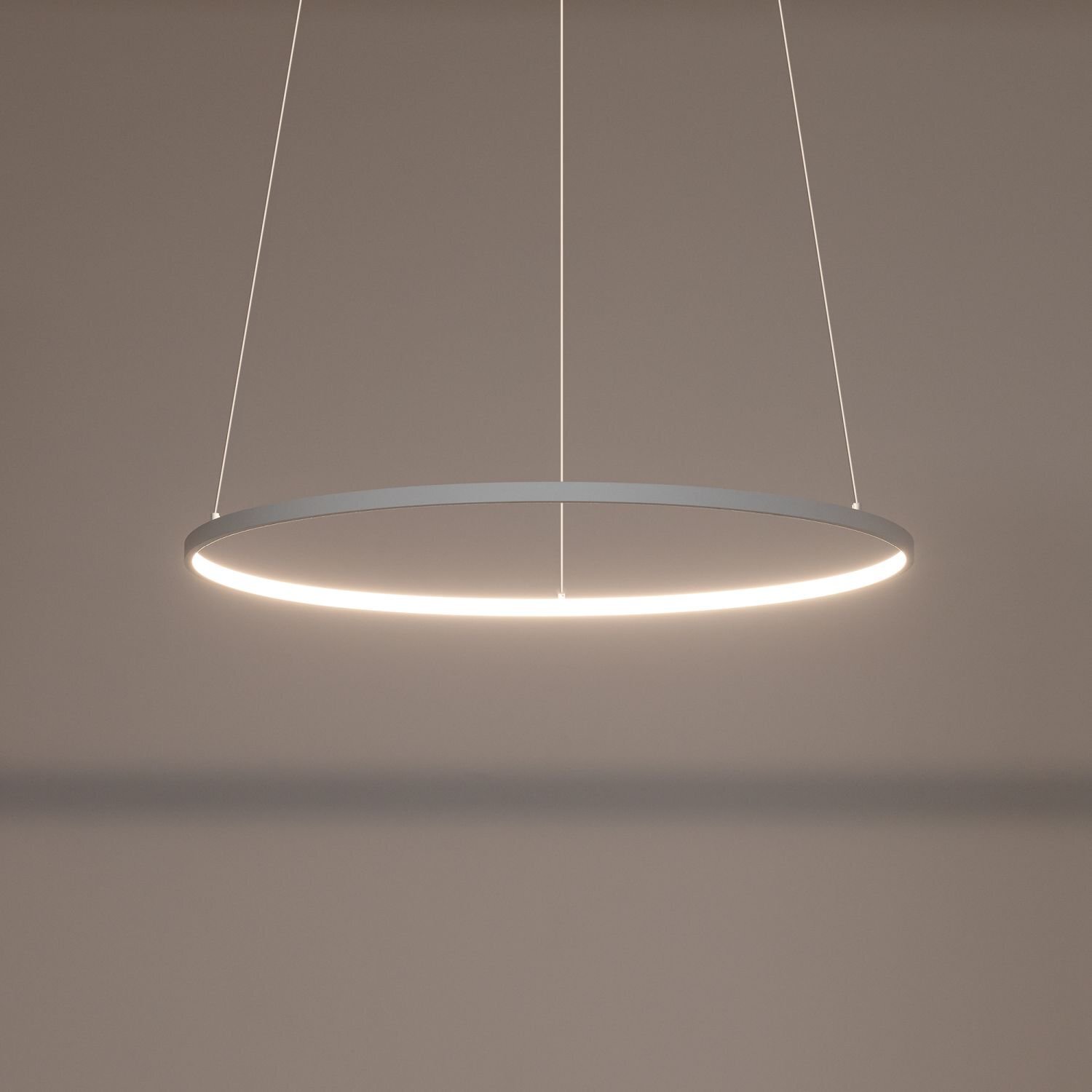 Na obrazie widoczna jest nowoczesna lampa wisząca w kształcie okręgu, emitująca jasne światło. Lampa zawieszona jest na dwóch cienkich przewodach na tle jednolitej, jasnej ściany.