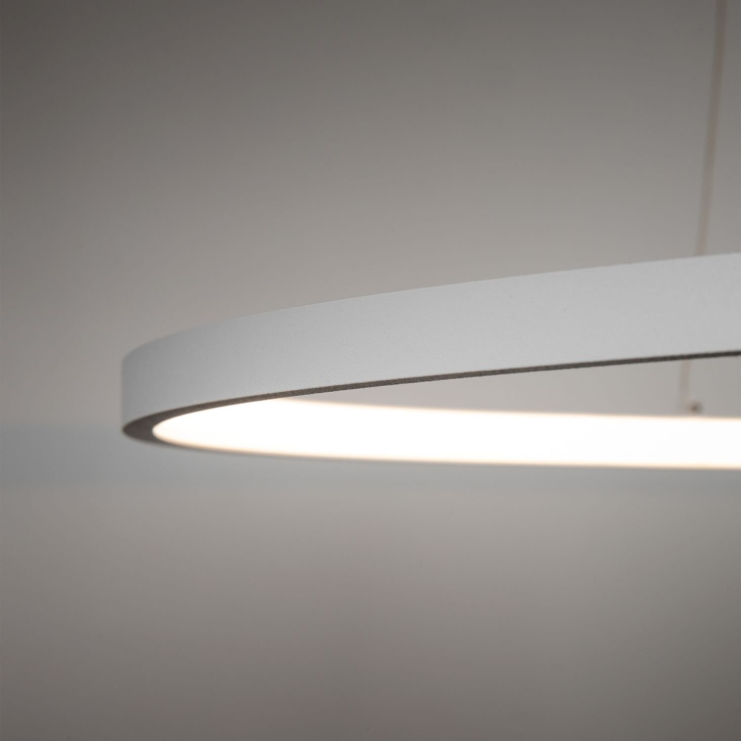 Obraz przedstawia fragment nowoczesnej, wiszącej lampy LED o okrągłym kształcie, emitującej jasne światło. Lampa ma gładką, matową powierzchnię w jasnym kolorze.