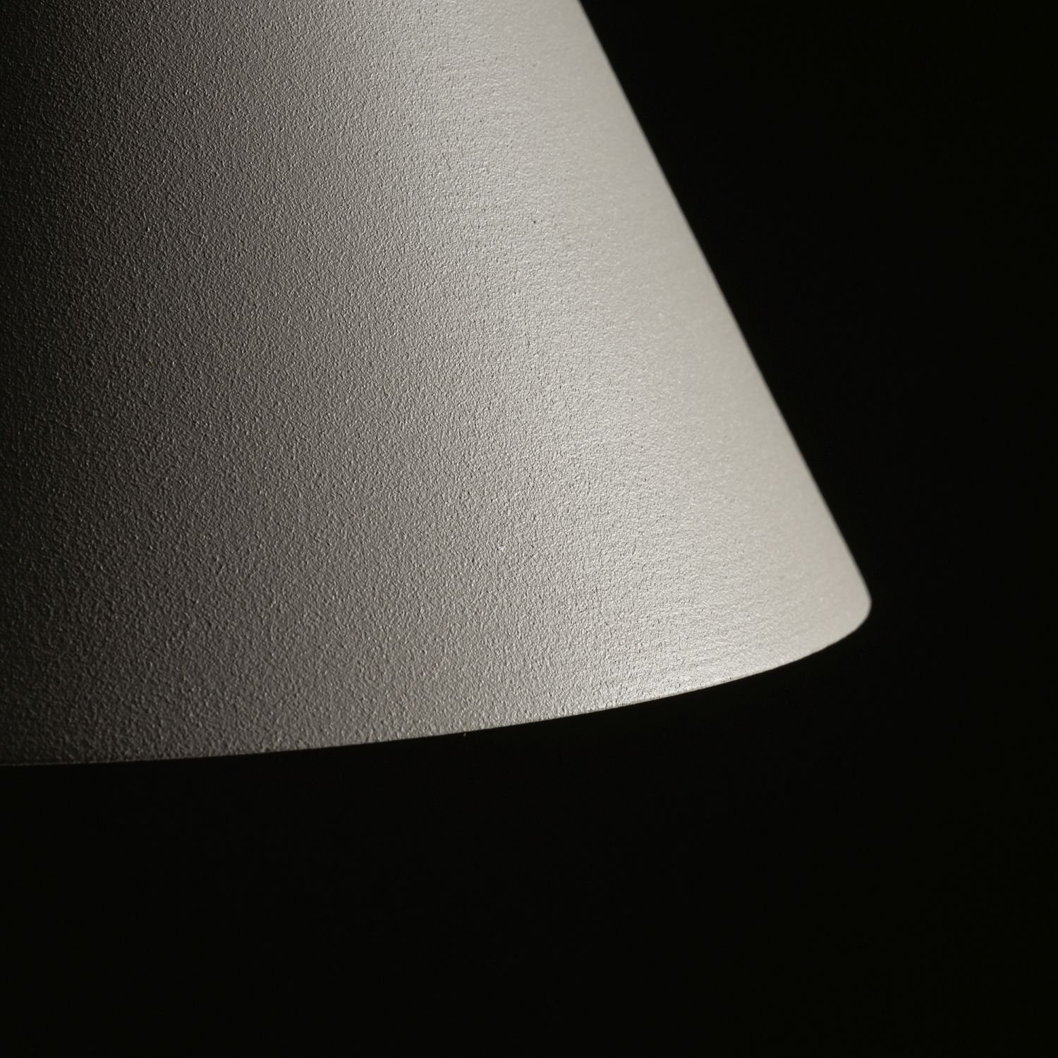 Obraz przedstawia zbliżenie na powierzchnię klosza lampy o teksturowanej, jasnej powierzchni. Tło jest ciemne, co podkreśla kontrast z kloszem.