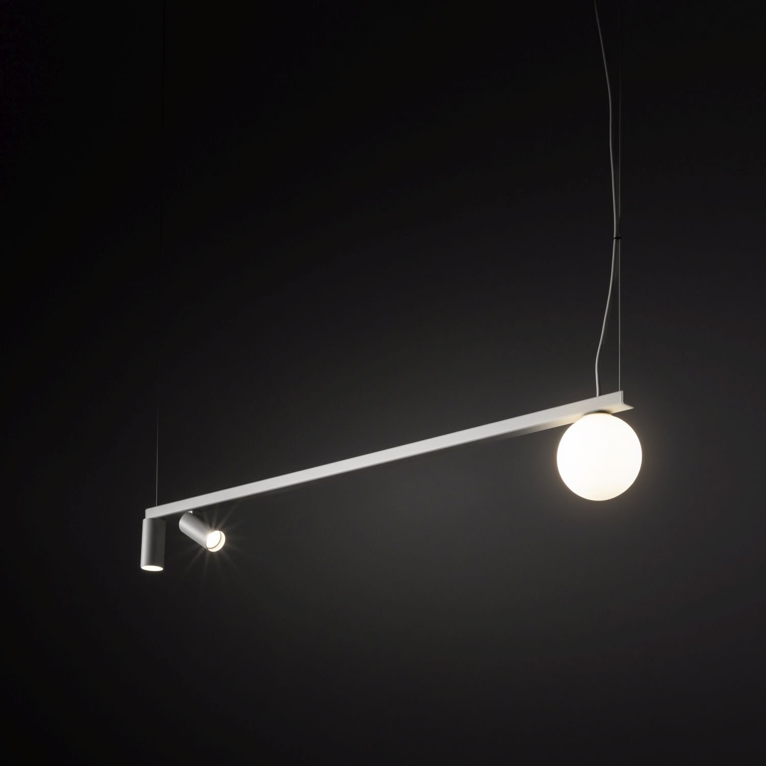 Nowoczesna lampa wisząca z reflektorkiem i kulistym kloszem, zawieszona na cienkich przewodach na tle ciemnego tła.
