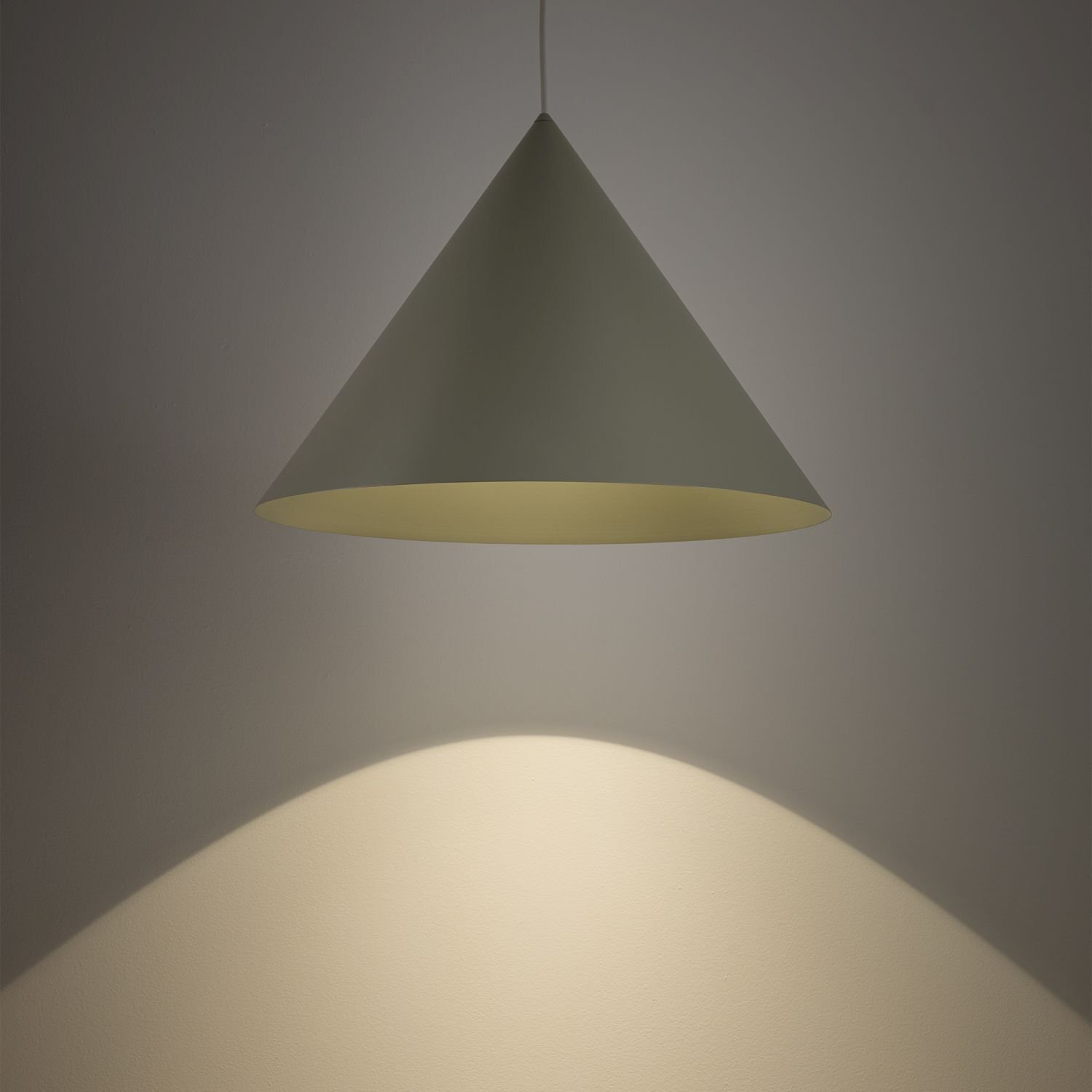 Na obrazie widoczna jest lampa wisząca w kształcie stożka, emitująca światło na ścianę poniżej. Światło tworzy jasny, rozproszony wzór na powierzchni.