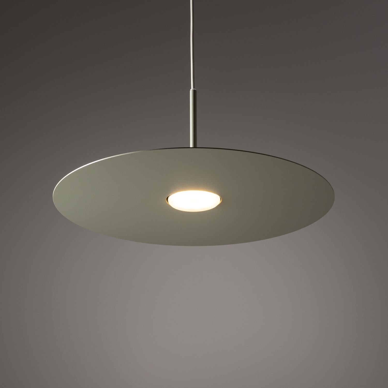 Na obrazie widoczna jest nowoczesna lampa wisząca z okrągłym, płaskim kloszem w kolorze szarym. Lampa emituje ciepłe, białe światło.