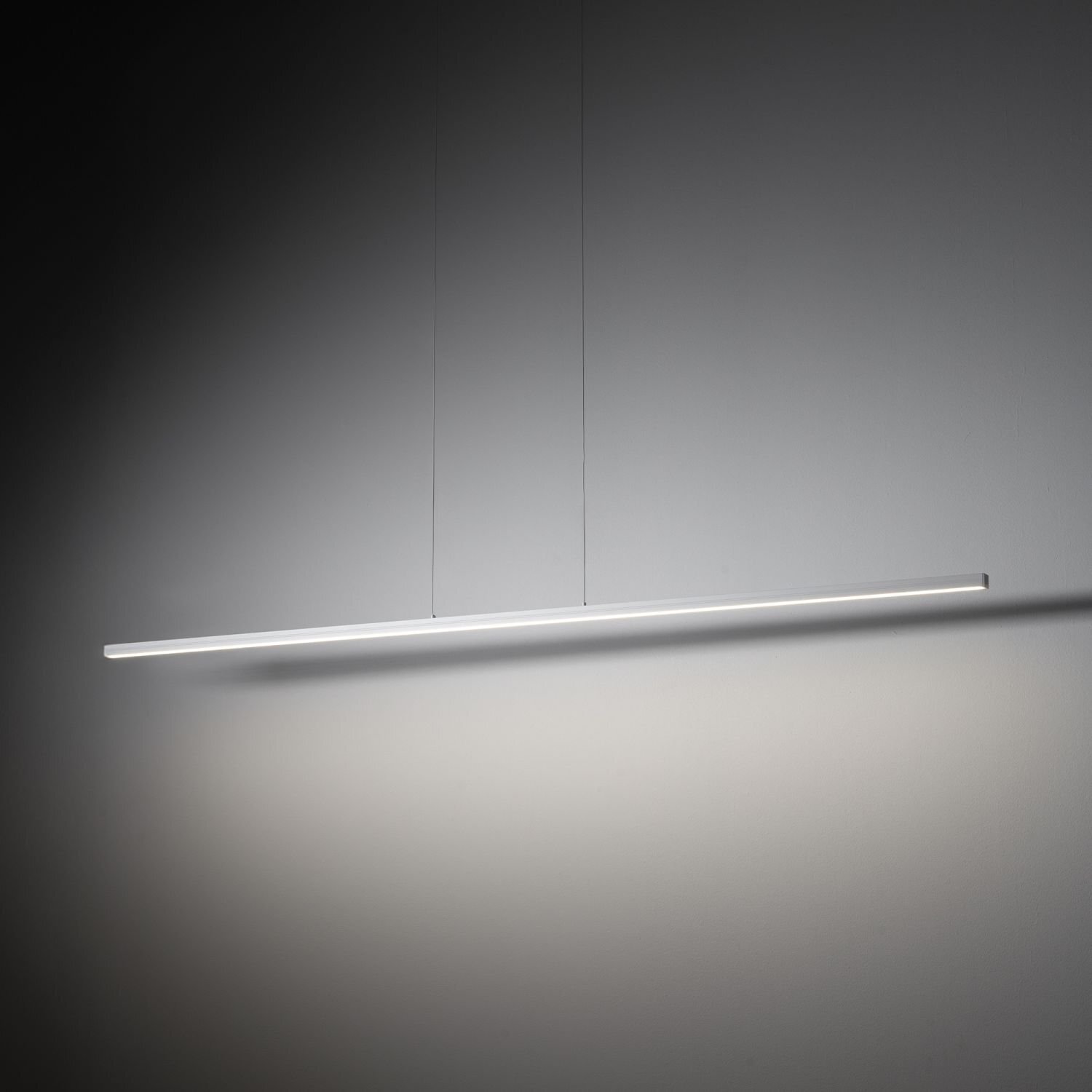 Nowoczesna lampa wisząca LED o prostym, liniowym kształcie, zawieszona na dwóch cienkich przewodach. Emituje jasne, równomierne światło na neutralnym tle.