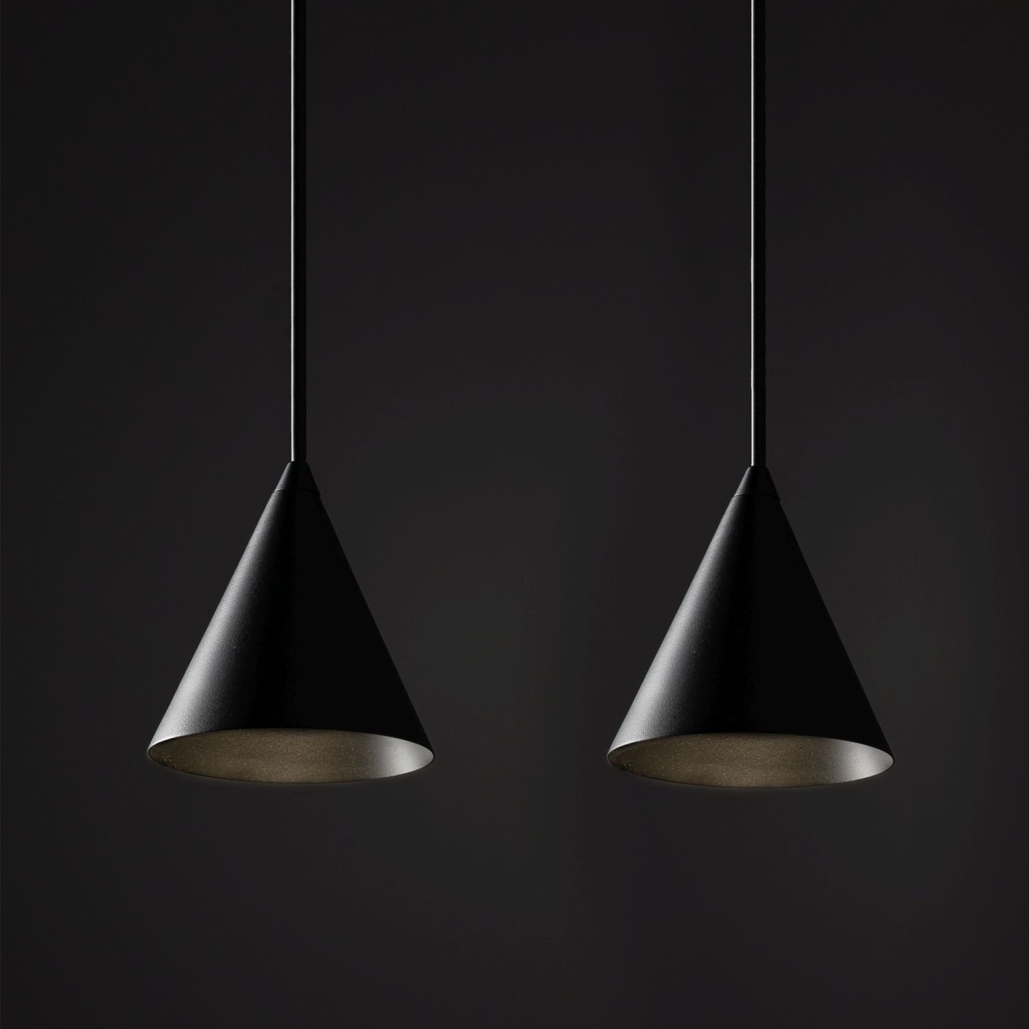 Na obrazie widoczne są dwie czarne, stożkowe lampy wiszące na ciemnym tle. Lampy mają gładką powierzchnię i są zawieszone na cienkich przewodach.