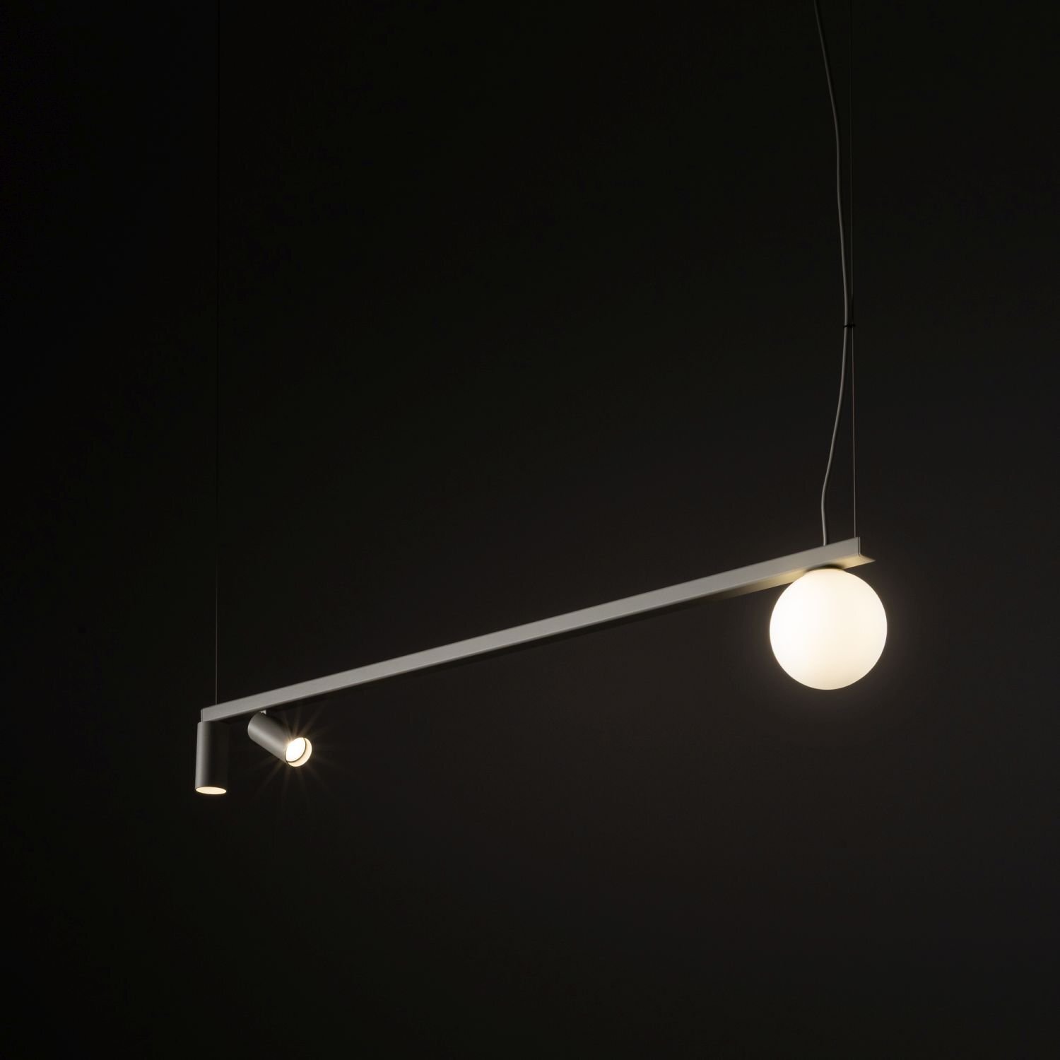 Na ciemnym tle wisi nowoczesna lampa sufitowa z reflektorkiem i kulistym kloszem. Lampa jest zawieszona na cienkim przewodzie.