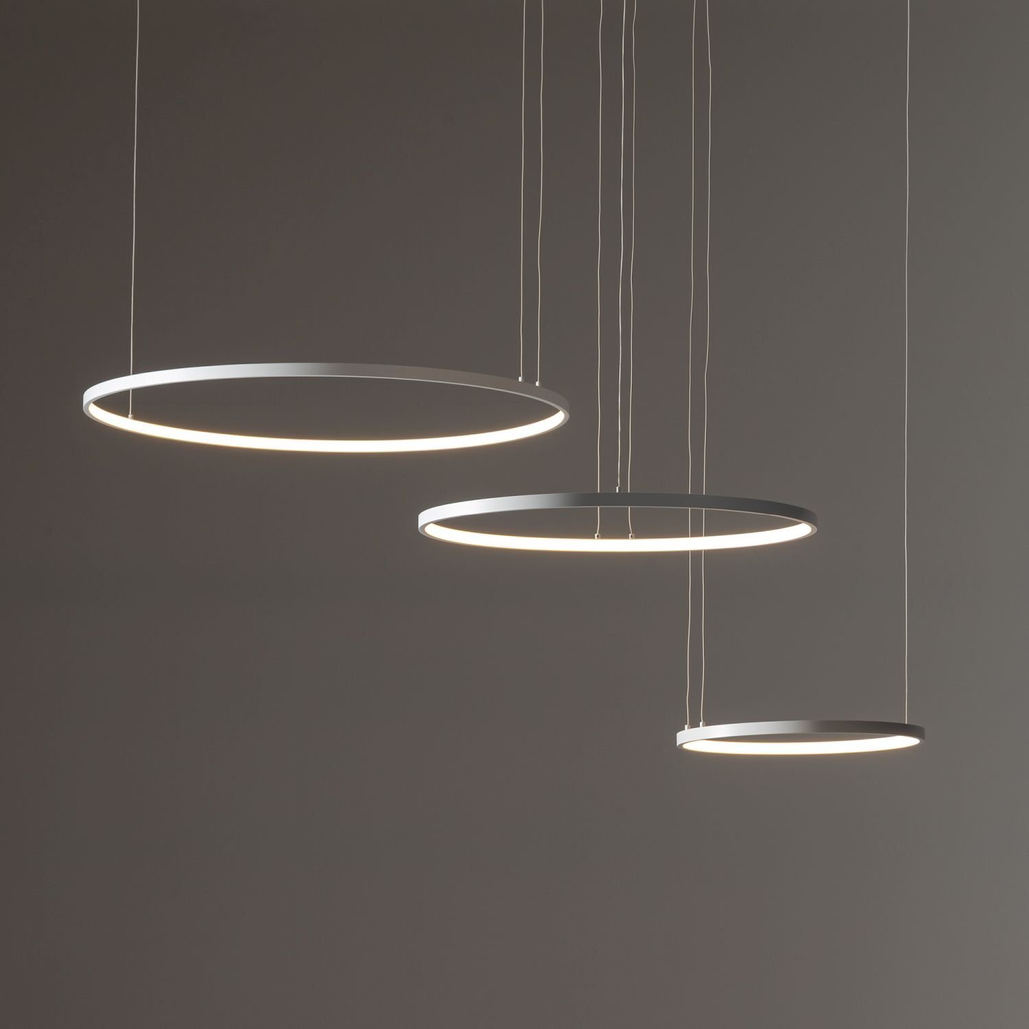 Na obrazie widoczne są trzy okrągłe, wiszące lampy LED o nowoczesnym designie, zawieszone na cienkich przewodach. Lampy emitują delikatne, białe światło.