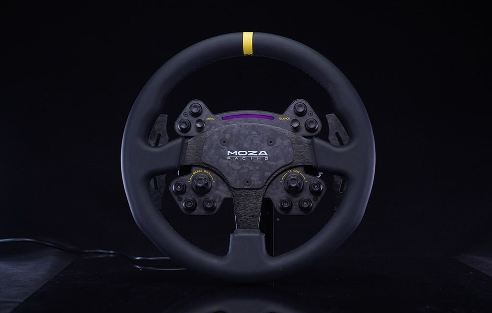 Na obrazie widoczna jest kierownica z logo \'MOZA Racing\' na środku, z kilkoma przyciskami i żółtym paskiem na górze. Tło jest ciemne, a kierownica ma nowoczesny design.