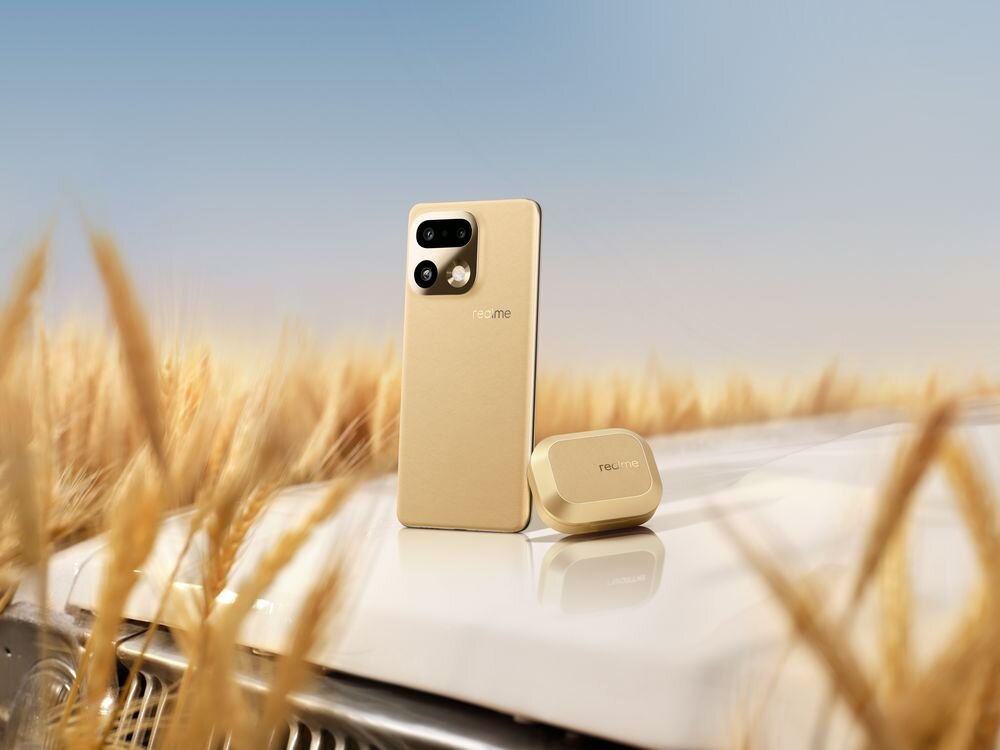 Złoty smartfon i etui na słuchawki z logo \'realme\' stoją na białej powierzchni, w tle widać pole zboża i niebo.