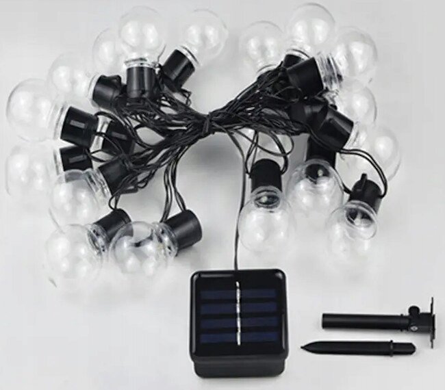 Na obrazie widoczna jest girlanda z przezroczystymi żarówkami LED oraz panel solarny z dwoma czarnymi elementami montażowymi. Żarówki są połączone czarnym przewodem, a panel ma widoczne paski ogniw słonecznych.