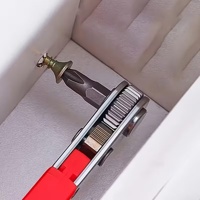 Na obrazie widoczna jest grzechotka z czerwonym uchwytem, która trzyma bit wkręcany w śrubę. Tło jest jasne i ma teksturę przypominającą materiał.