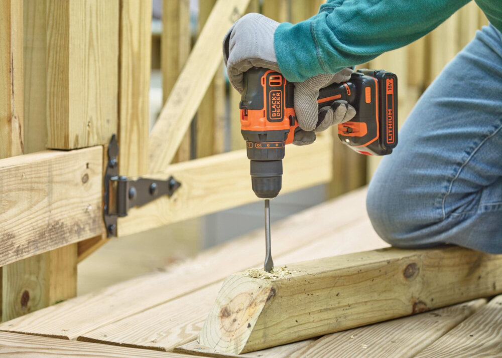 Osoba używa wiertarko-wkrętarki BLACK+DECKER do wiercenia w drewnianej belce. Na urządzeniu widoczne są napisy: \'BLACK+DECKER\' i \'LITHIUM\'.