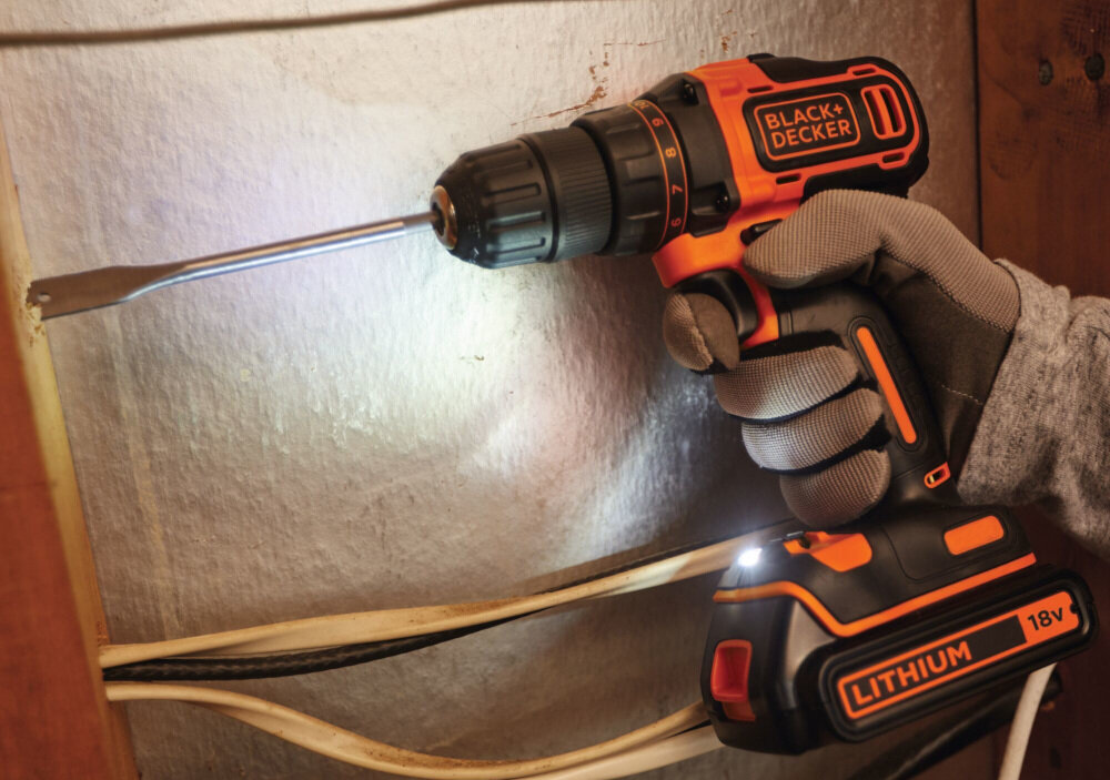 Osoba trzyma wiertarko-wkrętarkę BLACK+DECKER z widocznym logo, używaną do pracy przy drewnianej powierzchni. Na urządzeniu widoczny jest napis \'LITHIUM 18V\'.
