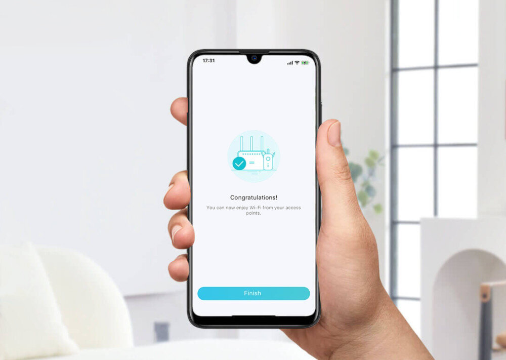 Osoba trzyma smartfon z ekranem wyświetlającym komunikat: \'Congratulations! You can now enjoy Wi-Fi from your access points.\' oraz przycisk \'Finish\'.