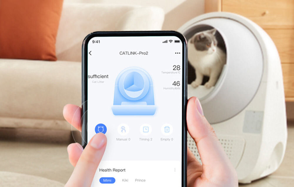 Osoba trzyma smartfon z aplikacją CATLINK–Pro2, pokazującą temperaturę 28°C i wilgotność 46%. W tle widać kota w okrągłej, białej kuwecie.