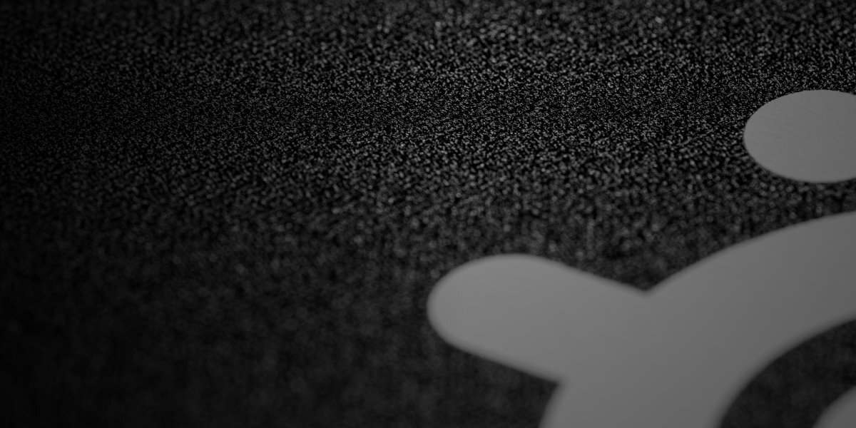 Zbliżenie na czarną powierzchnię z widoczną teksturą i fragmentem białego logo w kształcie okręgu z wypustkami.