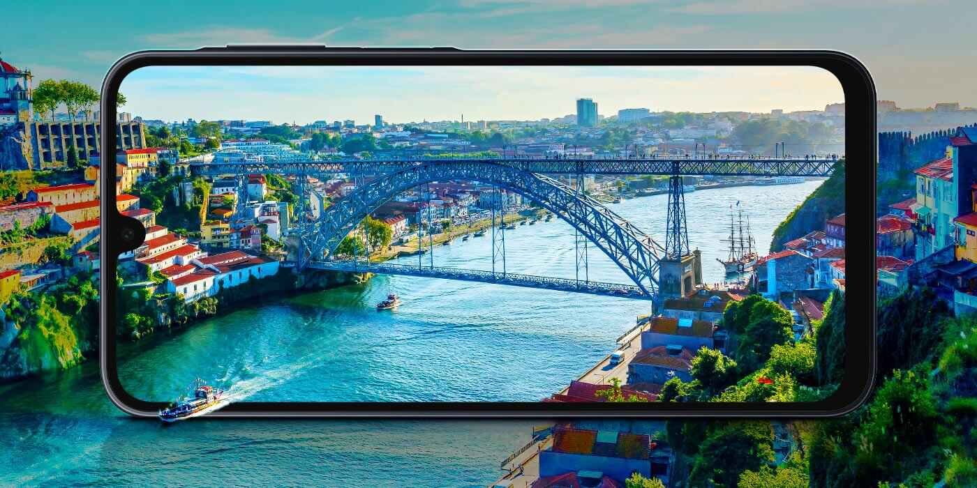 Samsung Galaxy A16 LTE z wyświetlaczem o przekątnej 6,7 cala dostępny w sklepach Media Expert Na obrazie widać smartfon z wyświetlaczem przedstawiającym most nad rzeką w mieście. W tle za smartfonem znajduje się ten sam widok, co na ekranie urządzenia.