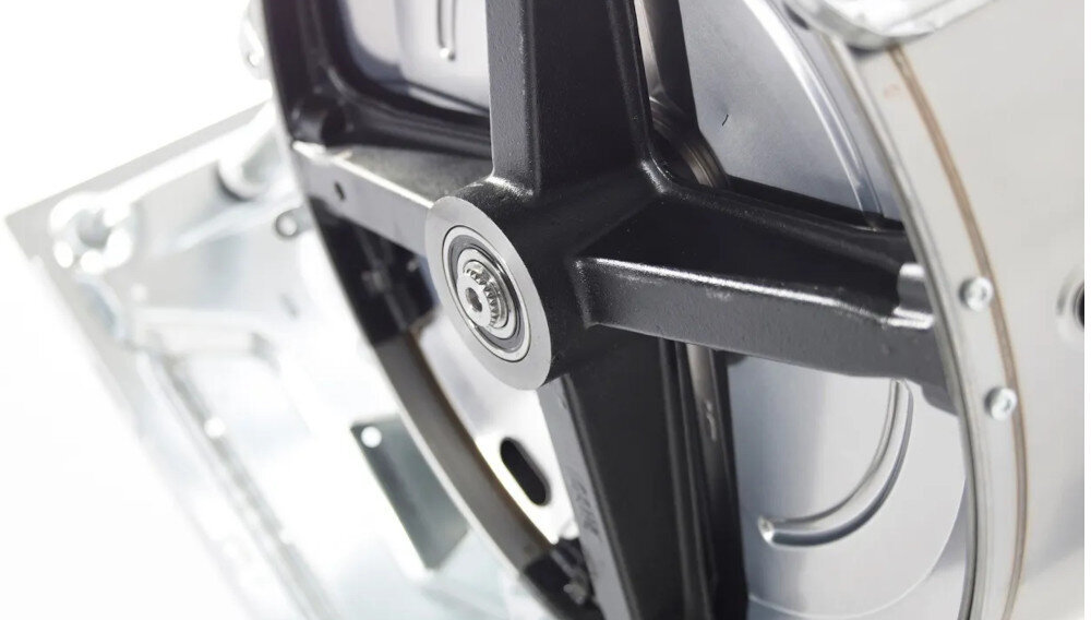 Zbliżenie na metalowy mechanizm pralki z widocznym czarnym ramieniem i centralnym łożyskiem. Elementy są wykonane z metalu i mają srebrzysty kolor.