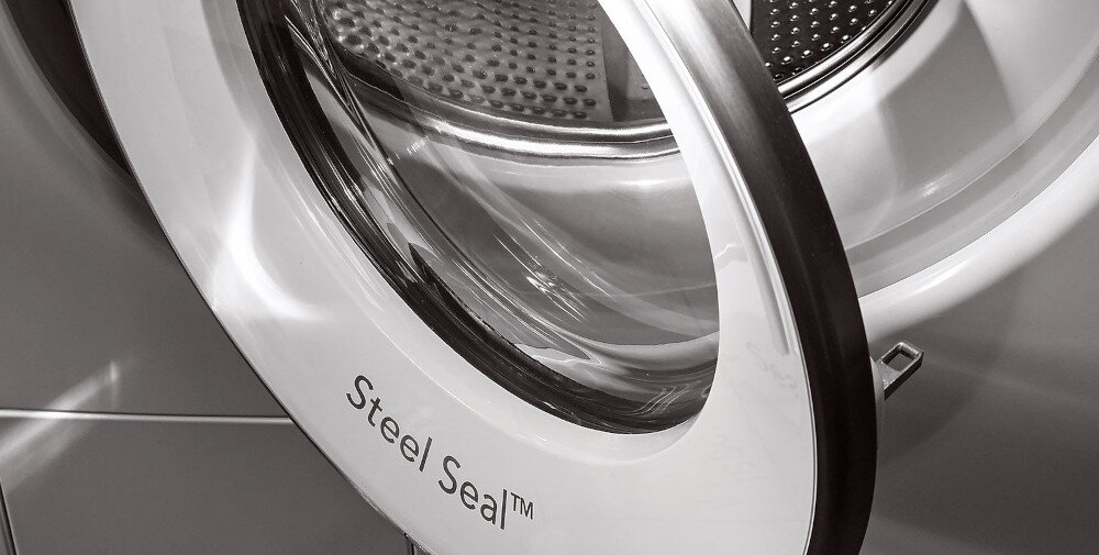 Zdjęcie przedstawia otwarte drzwi pralki z napisem \'Steel Seal™\' na białej ramie. W tle widoczny jest bęben pralki.