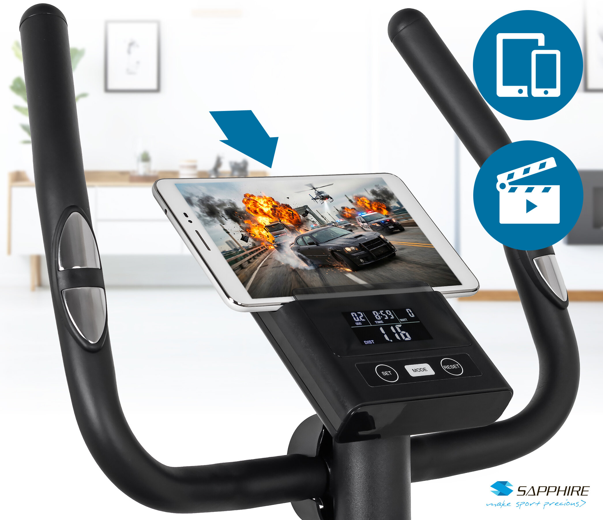 Rower treningowy z uchwytem na tablet, na którym wyświetlany jest film akcji z samochodami i eksplozjami. Na panelu sterowania widoczne są przyciski i wyświetlacz z danymi treningowymi, a w rogu znajduje się logo \'SAPPHIRE make sport precious\'.